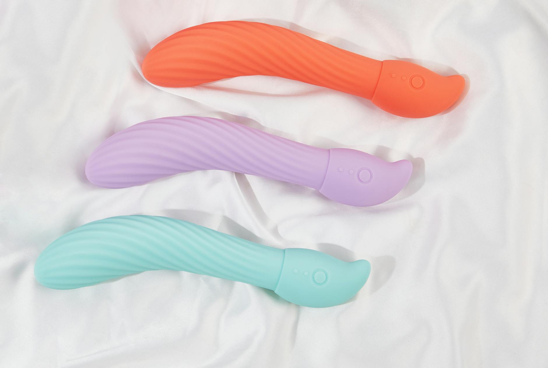 Hand holding an orange vibrator against a minimalistic purple backdrop
