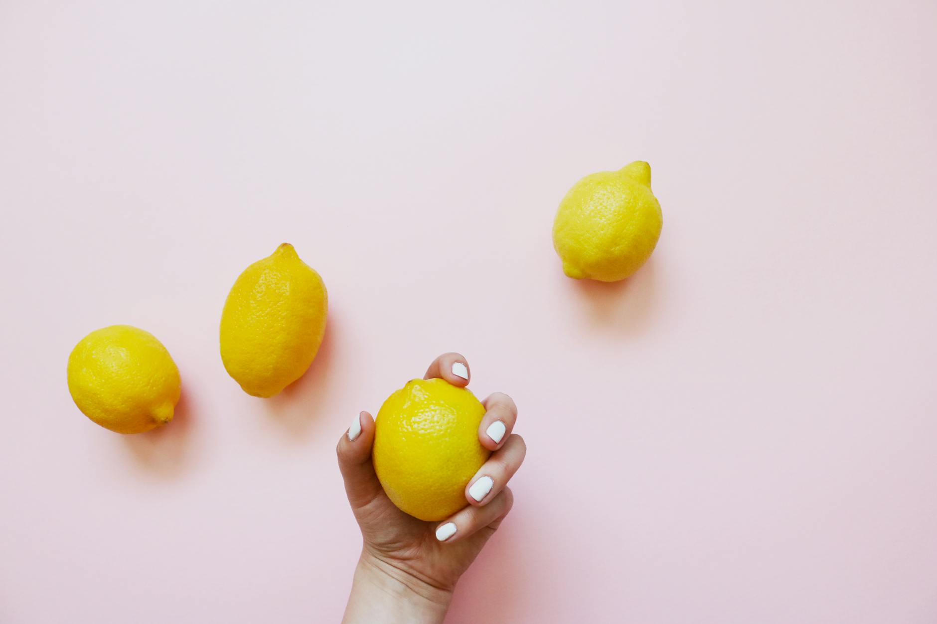A hand holding a fresh lemon on a soft pink background, symbolizing sensitivity and restored sensation