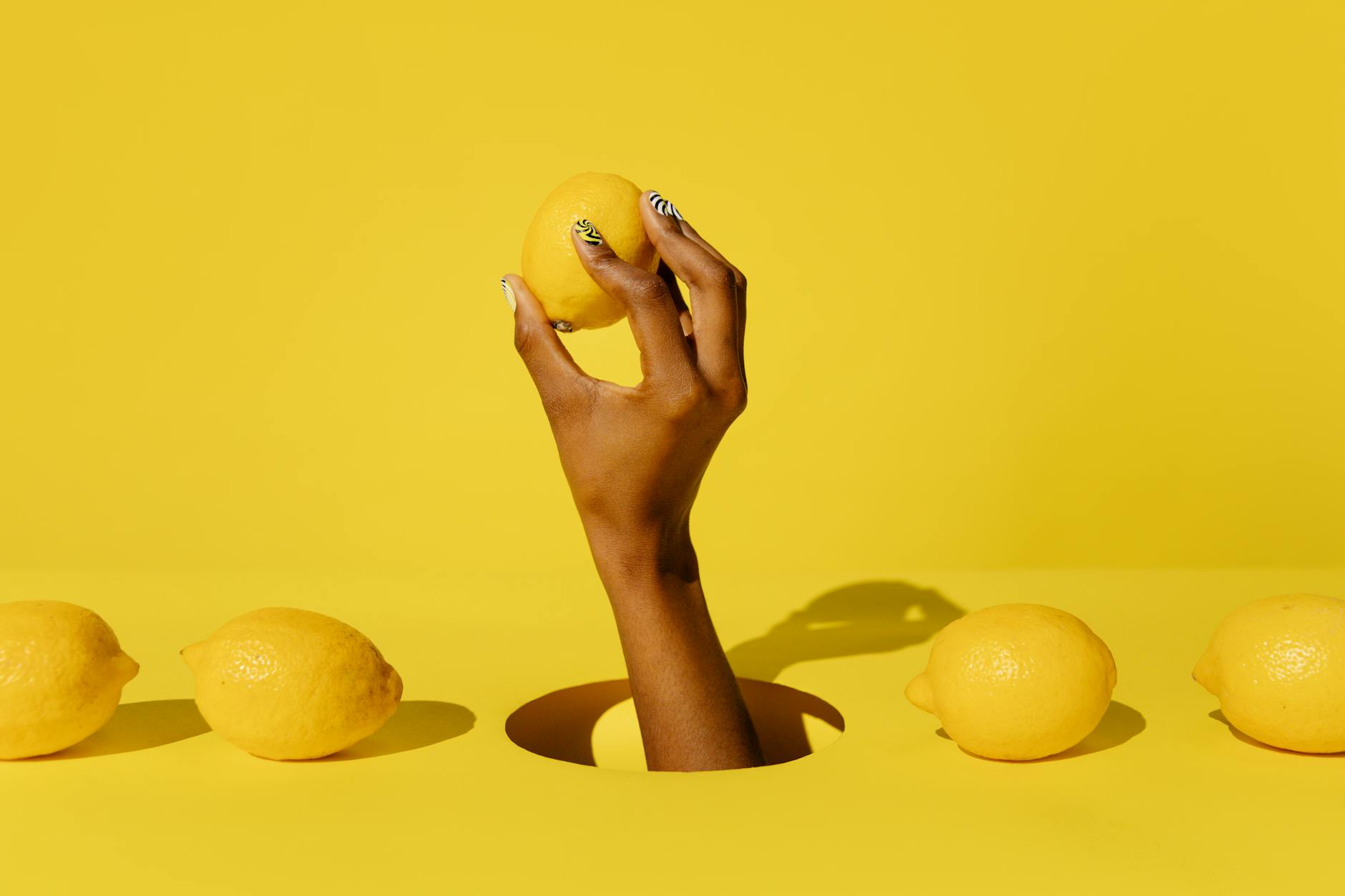 A hand holding a fresh lemon against a vivid yellow background, symbolizing the gentle intensity of lemon vibrators