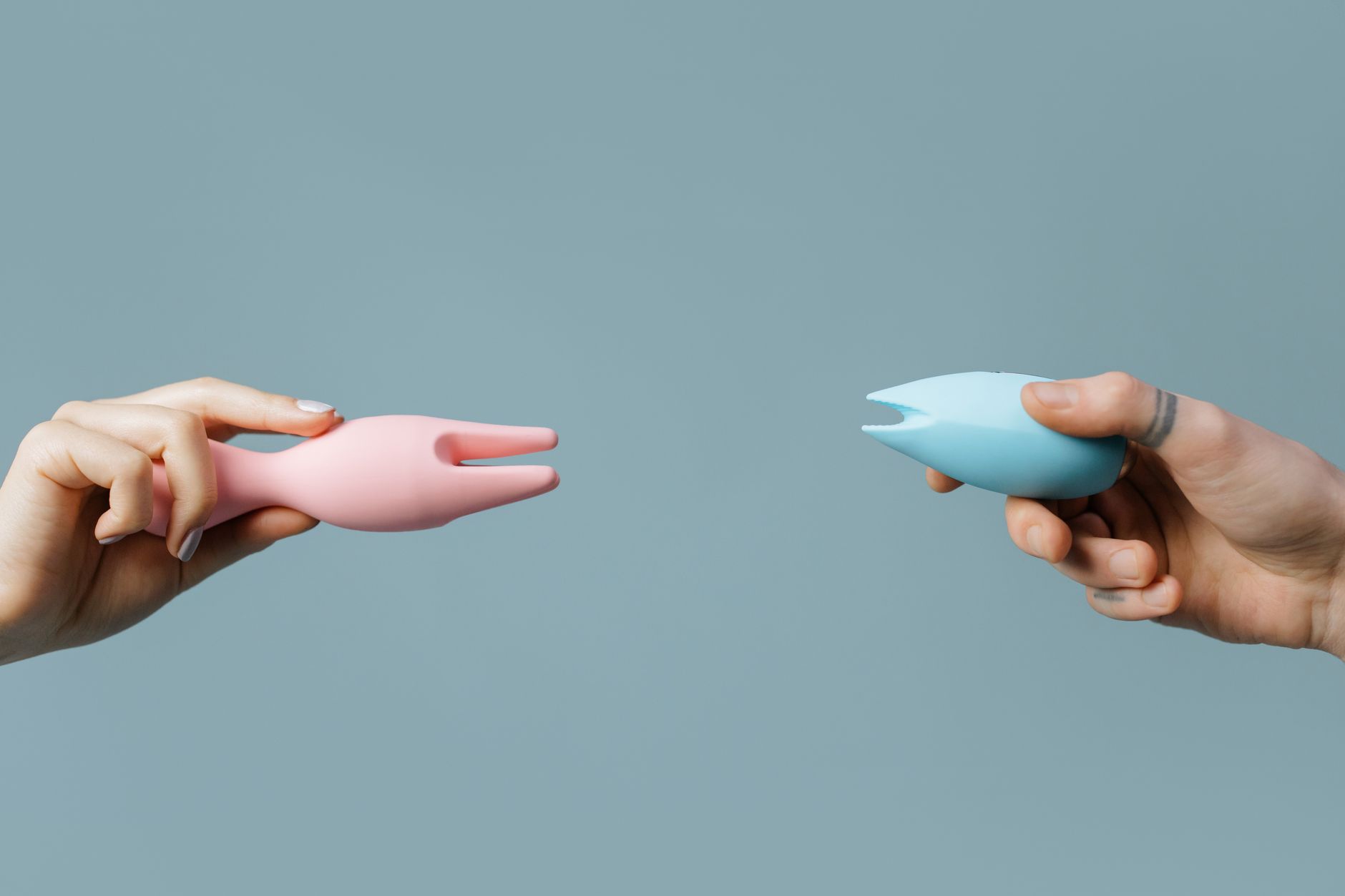 Two hands holding pink and blue lemon vibrators against a pastel background, representing diverse pleasure options during medication transitions.