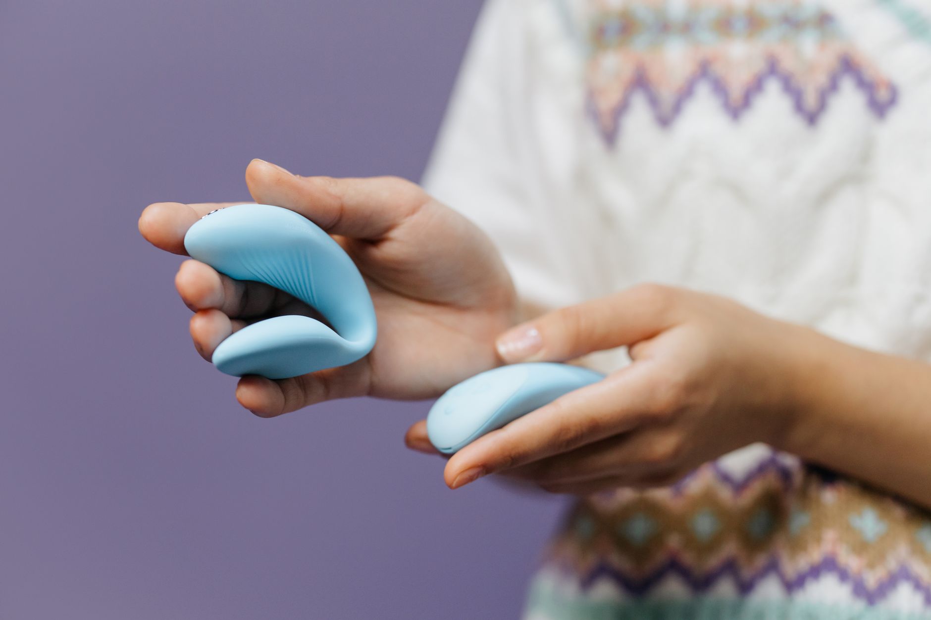 Hand holding a blue silicone clitoral vibrator against a purple background