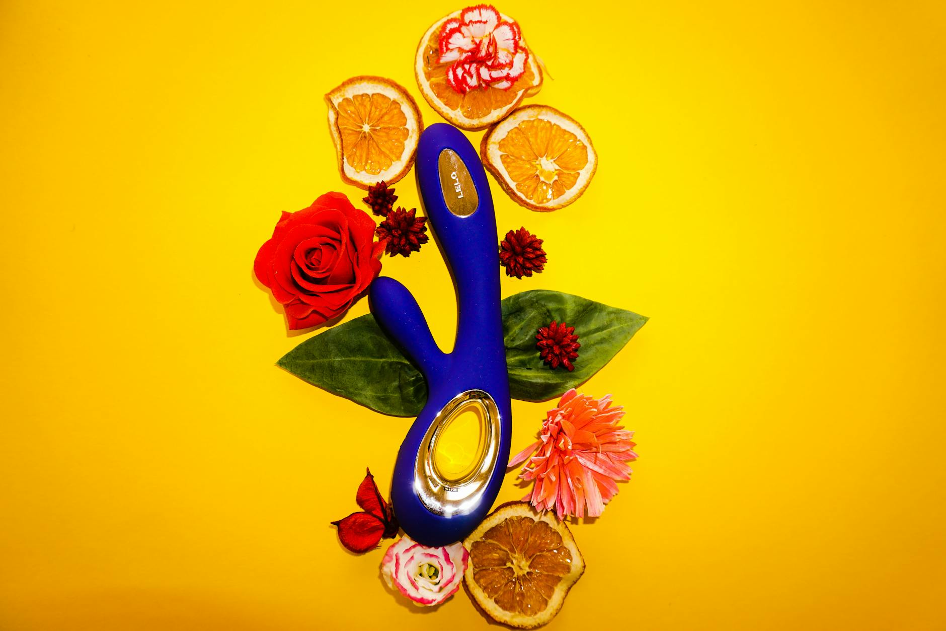 A sleek blue lemon vibrator surrounded by fresh citrus and flowers on a bright background