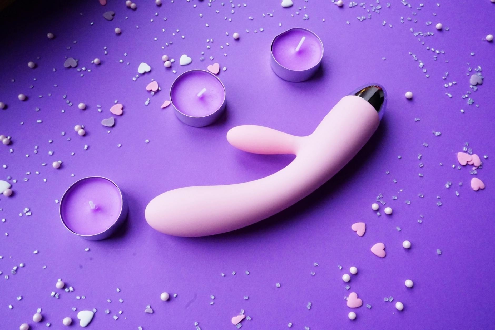 Pink clitoral vibrator on purple background with heart confetti and candles